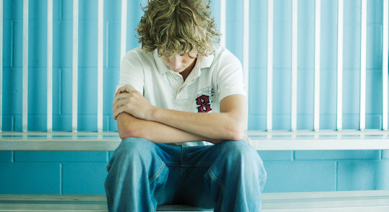 A boy sitting down and staring at his lap sadly